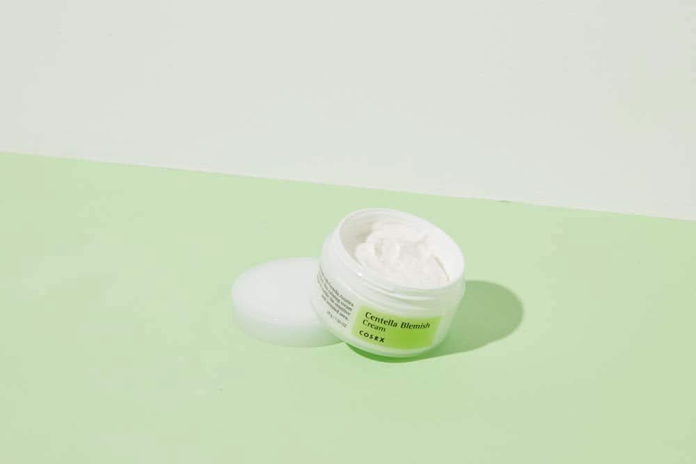 A jar of COSRX Centella Blemish Cream 30ml sitting on a green surface.