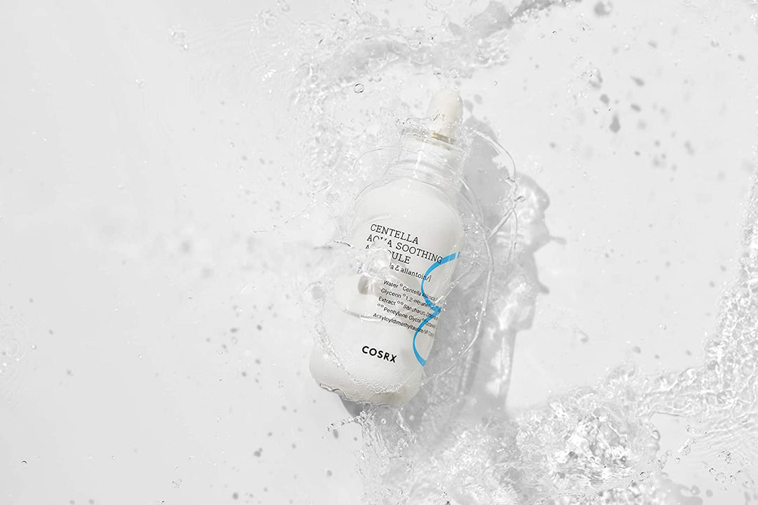En flaska COSRX Centella Aqua Soothing Ampoule 40ml som stänker på en vit yta, minskar rodnad och ger lugnande återfuktning.