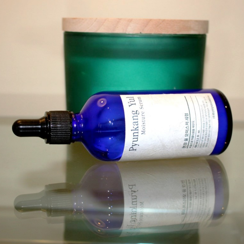 A bottle of Pyunkang Yul Moisture Serum 100ml balances the moisture levels on a table next to a candle.
